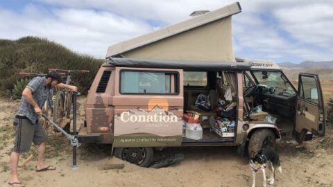 Dan's overland van is shown in the desert, with mountains in the background