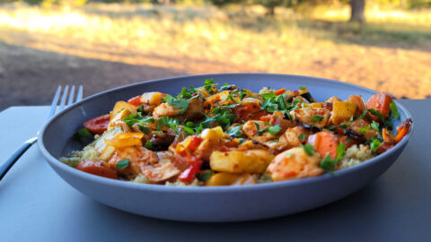 Harissa spiced vegetables and couscous is shown plated on a table.