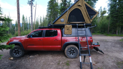 The CVT Mt. Hood rooftop tent is shown in khaki set up on a red pickup truck in the Colorado wilderness.