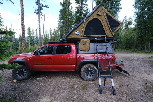 The CVT Mt. Hood rooftop tent is shown in khaki set up on a red pickup truck in the Colorado wilderness.
