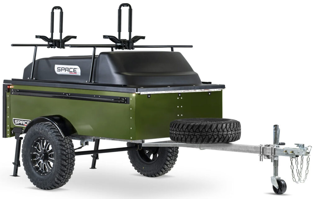 A green SPACE trailer is shown with a cap, closed, with a kayak rack on top against a white background