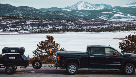 A closed SPACE trailer is shown hitched behind a green truck in winter, with snow capped mountains in the background