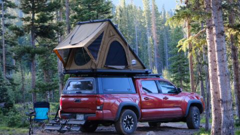 A red Toyota Tacoma is shown with a rooftop tent and a slightly sagging suspension.