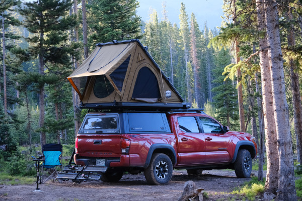 A red Toyota Tacoma is shown with a rooftop tent and a slightly sagging suspension.