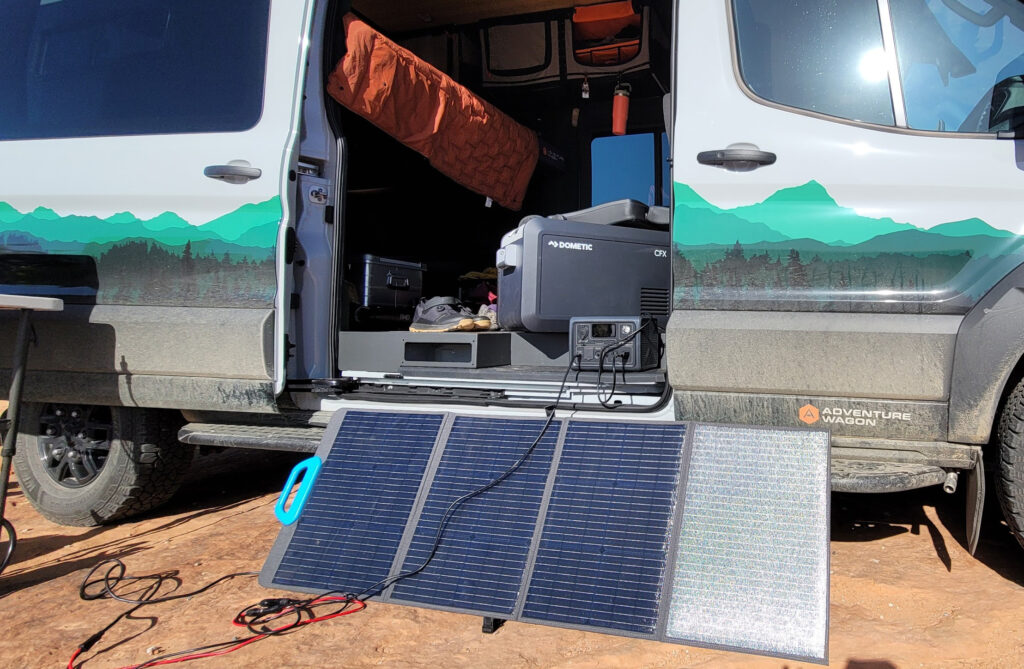 Overland campervan with the doors open and a solar panel charging setup showing.