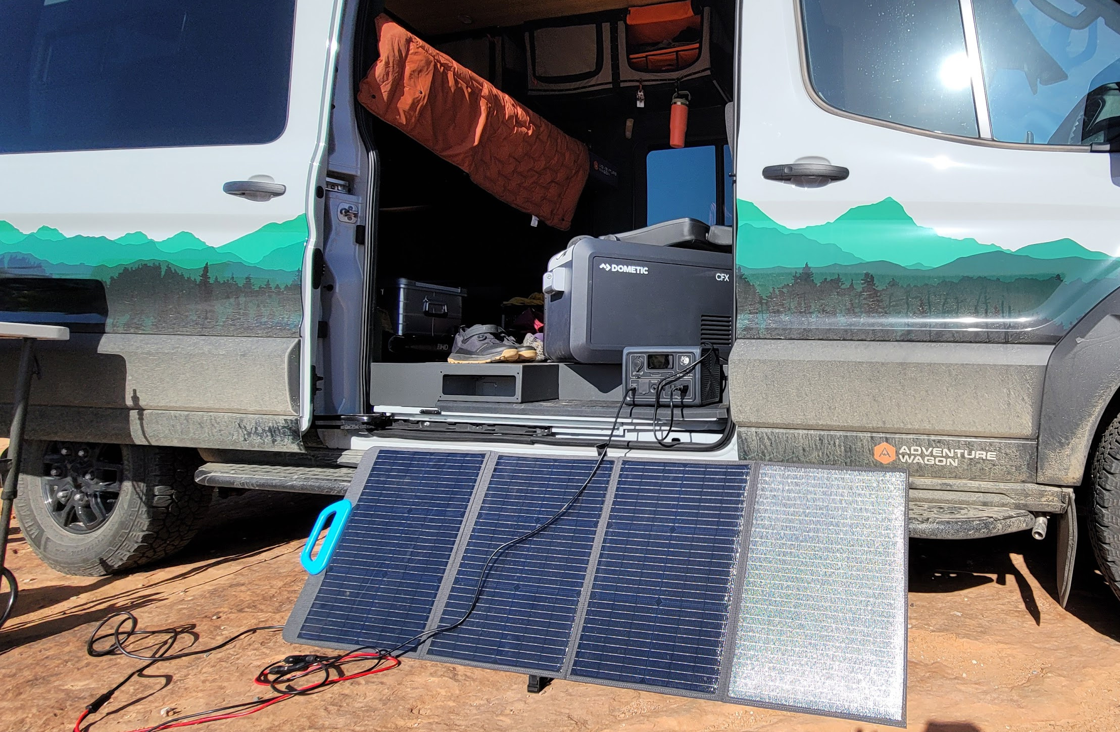 Overland campervan with the doors open and a solar panel charging setup showing