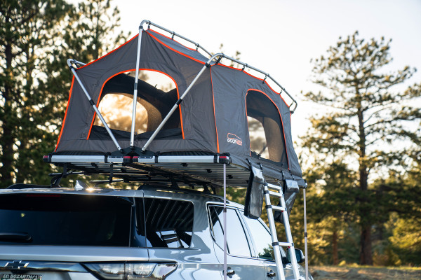 Meadowlark XL Roofnest car-top tent in gray with orange trim is shown, set up over an SUV as the sun sets behind the trees in the background